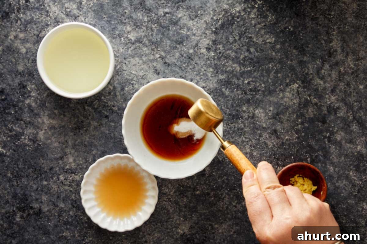 Hand adding sugar to soy sauce mixture in a white bowl with small bowls of vinegar and ginger.