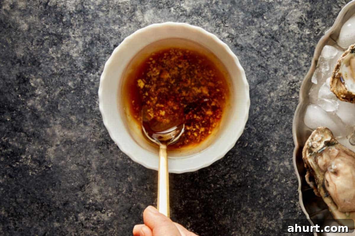 Bowl of soy sauce and ginger mixture being stirred with a spoon next to oysters on ice.