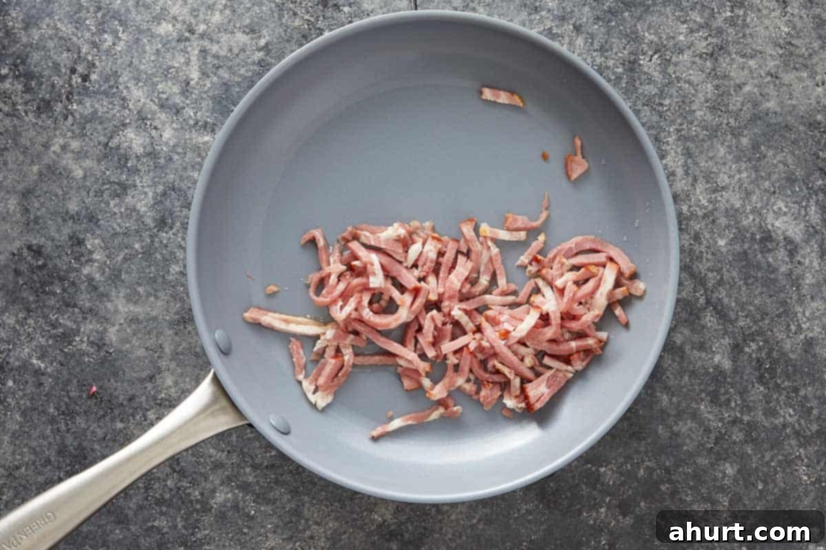 Crispy bacon strips cooking in a gray skillet.
