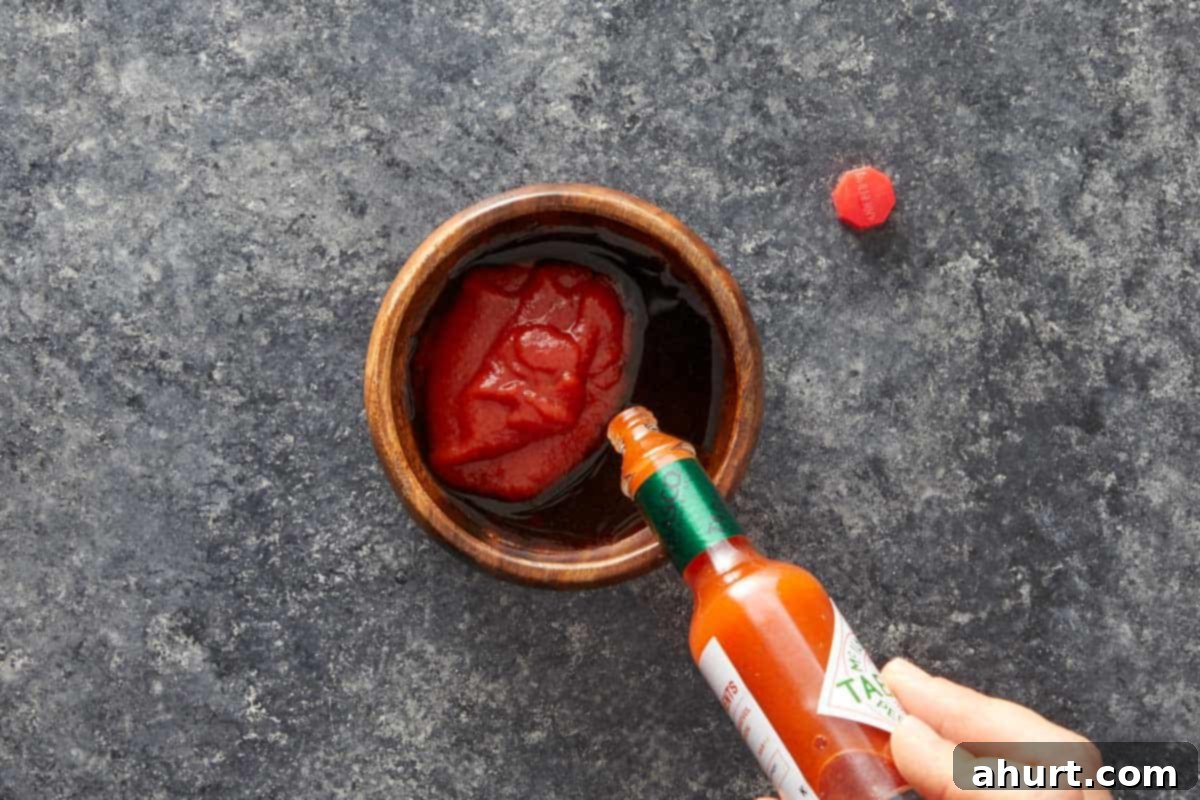 Hand pouring Tabasco sauce into a bowl of tomato sauce.