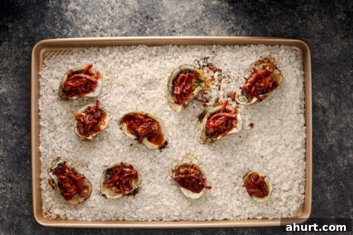 Baked oysters topped with bacon and sauce on a tray of rock salt.