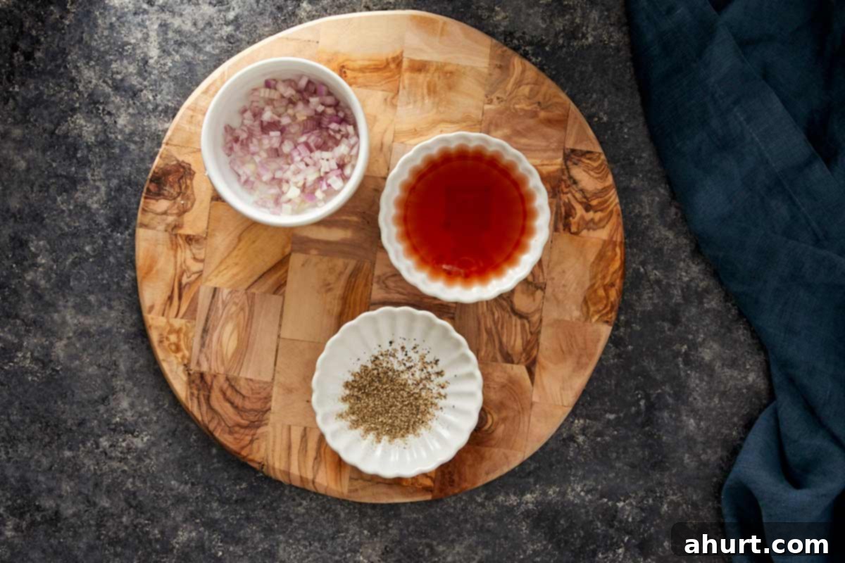 Small bowls with chopped shallots, red wine vinegar, and ground pepper on a wooden board.