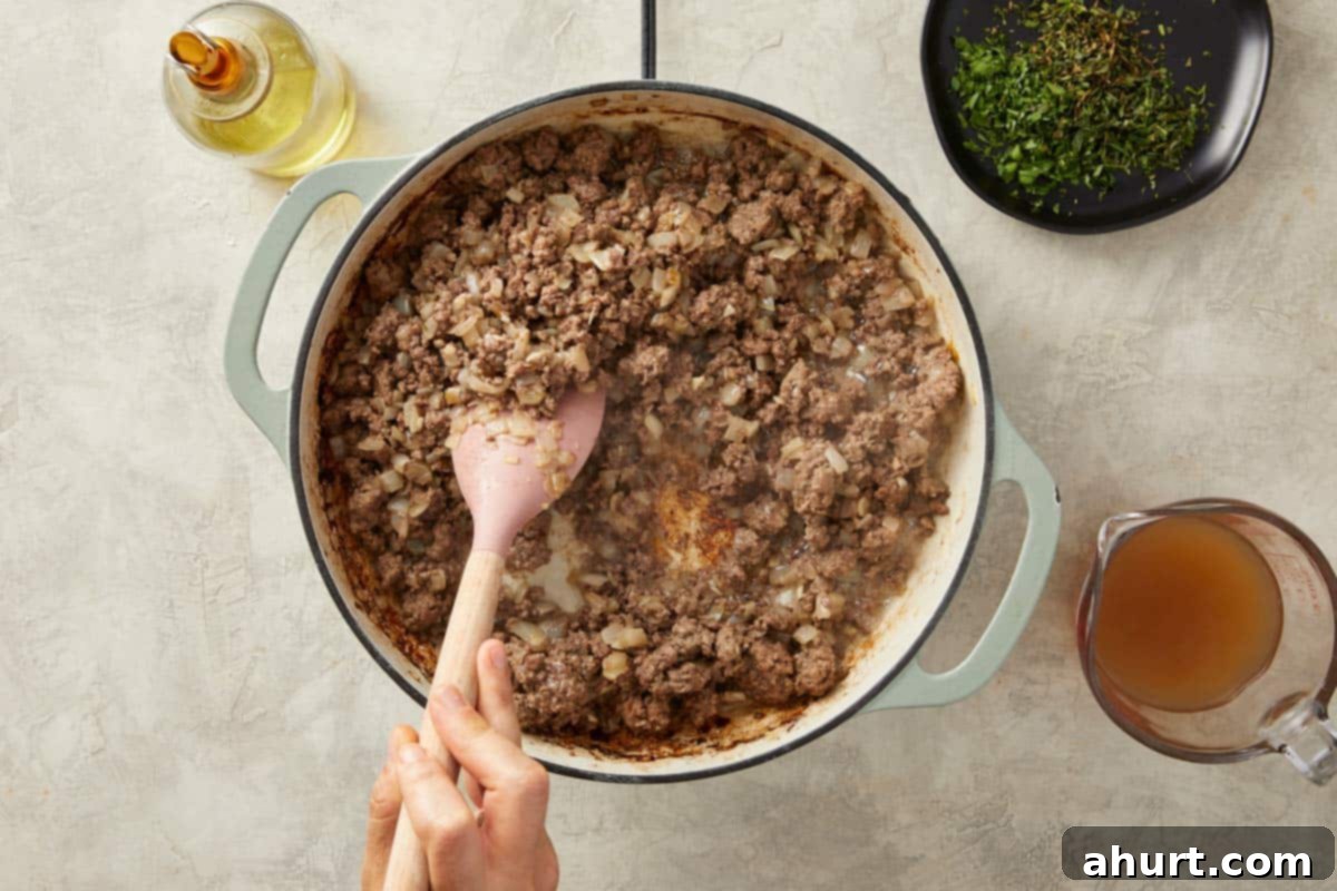 Ground beef browning in a skillet, meticulously broken apart with a spoon to ensure even cooking and the development of rich, caramelized flavor.