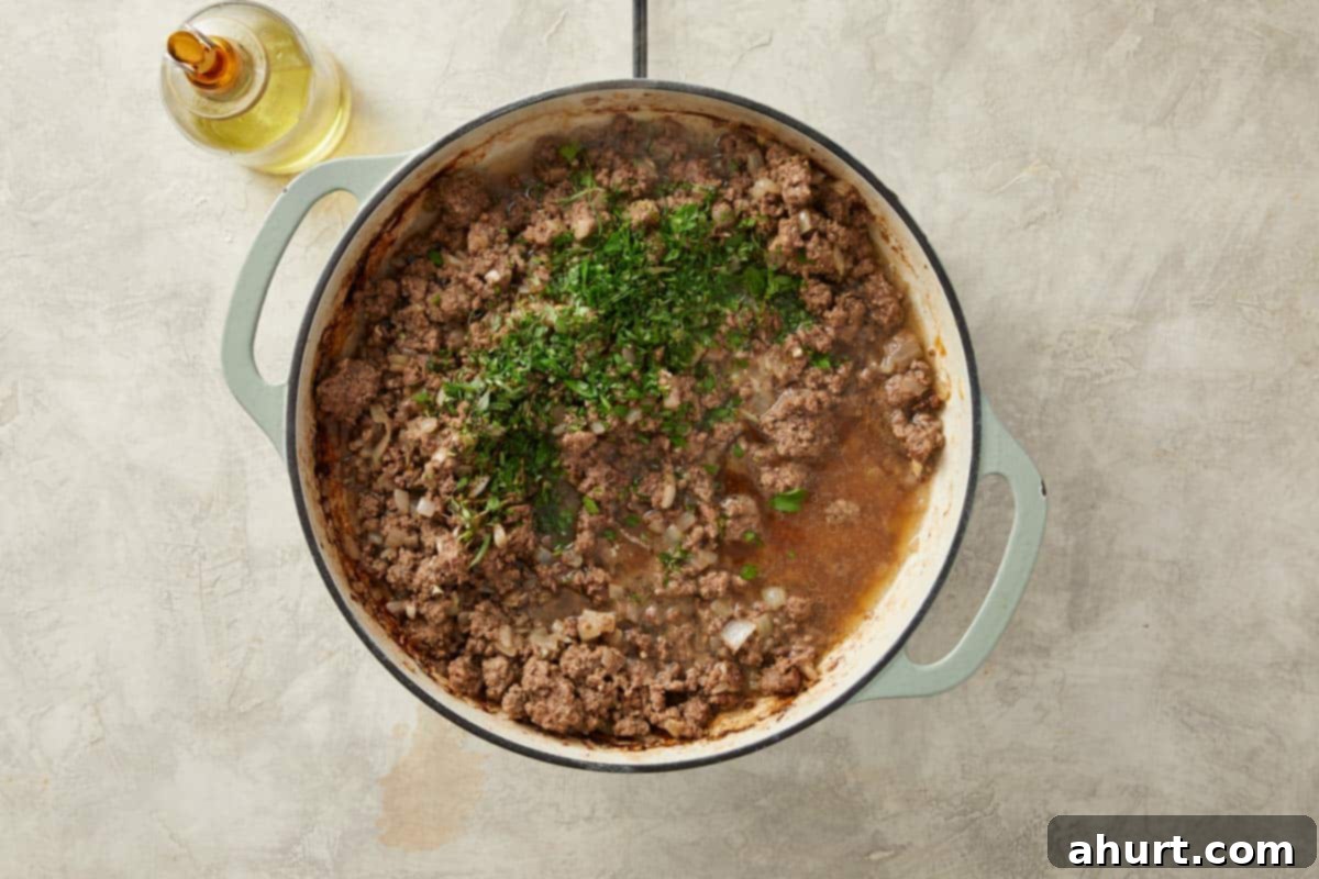 The savory meat sauce simmering gently with beef stock and a medley of fresh herbs, reducing slightly to concentrate its rich flavors.