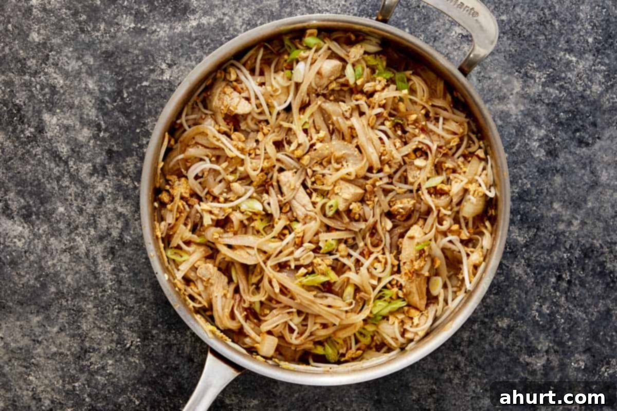 A pan filled with freshly cooked Pad Thai, showcasing the harmonious blend of chicken, tofu, eggs, bean sprouts, and noodles, ready to be served.