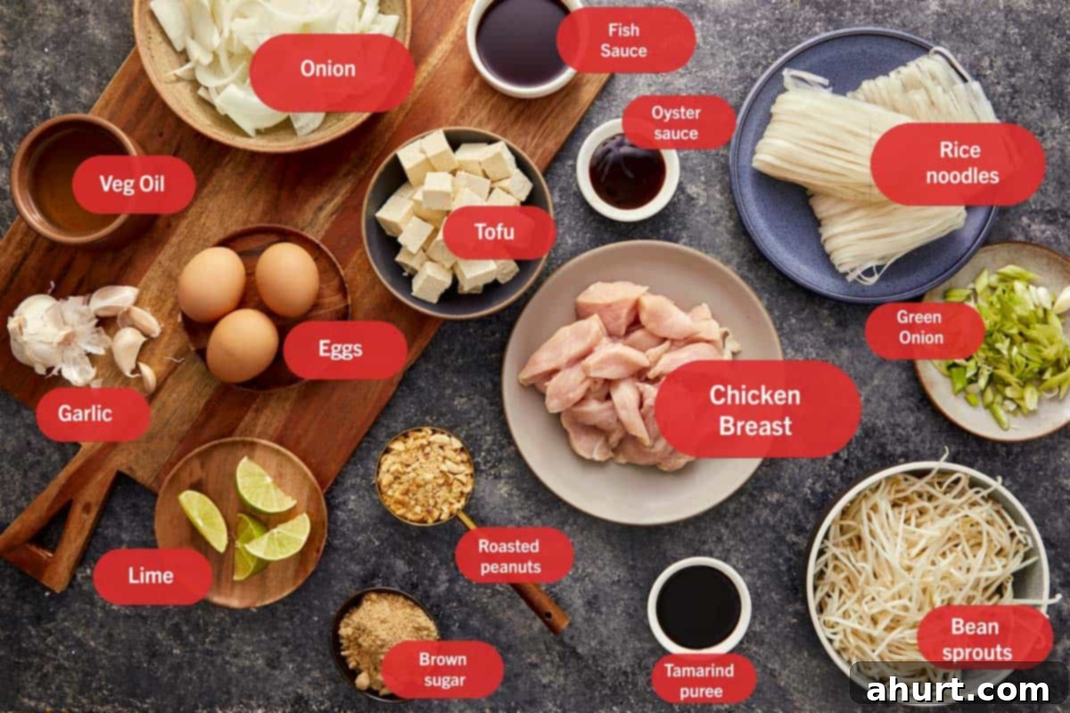 An overhead flat lay showing all the fresh ingredients for Pad Thai, including minced chicken breast, uncooked rice noodles, firm tofu cubes, raw eggs, sliced onion, minced garlic, fresh bean sprouts, chopped peanuts, tamarind puree, bottles of fish and oyster sauce, and vibrant lime wedges, arranged neatly with red labels.