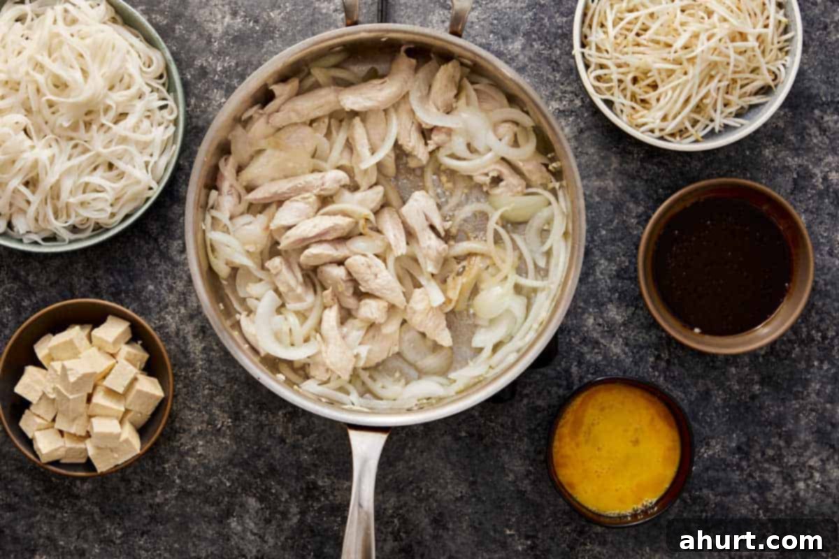 Minced chicken cooking in a hot wok with stir-fried onions and garlic, beginning to brown and mingle with the aromatics for Pad Thai.