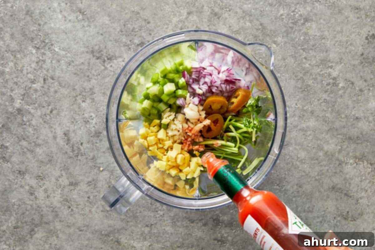 Blender filled with fresh ginger, garlic, celery, onion, coriander stems, jalapeño, and hot sauce.
