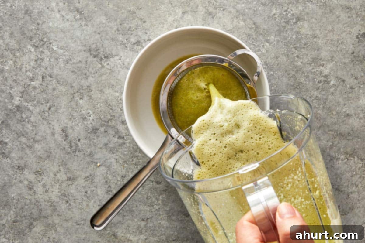Straining the blended marinade through a fine mesh sieve into a bowl.