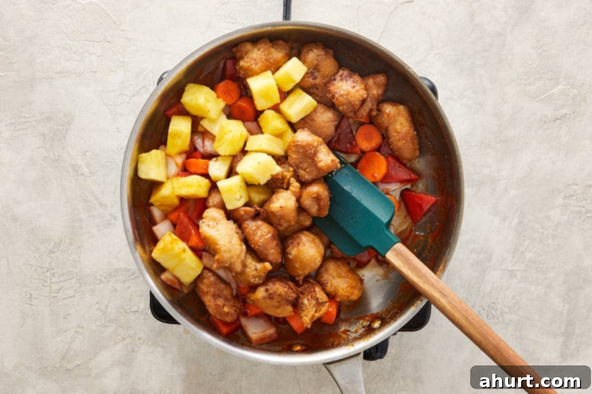 Wok with fried chicken, pineapple, carrots, onion, and bell pepper mixed with sauce.