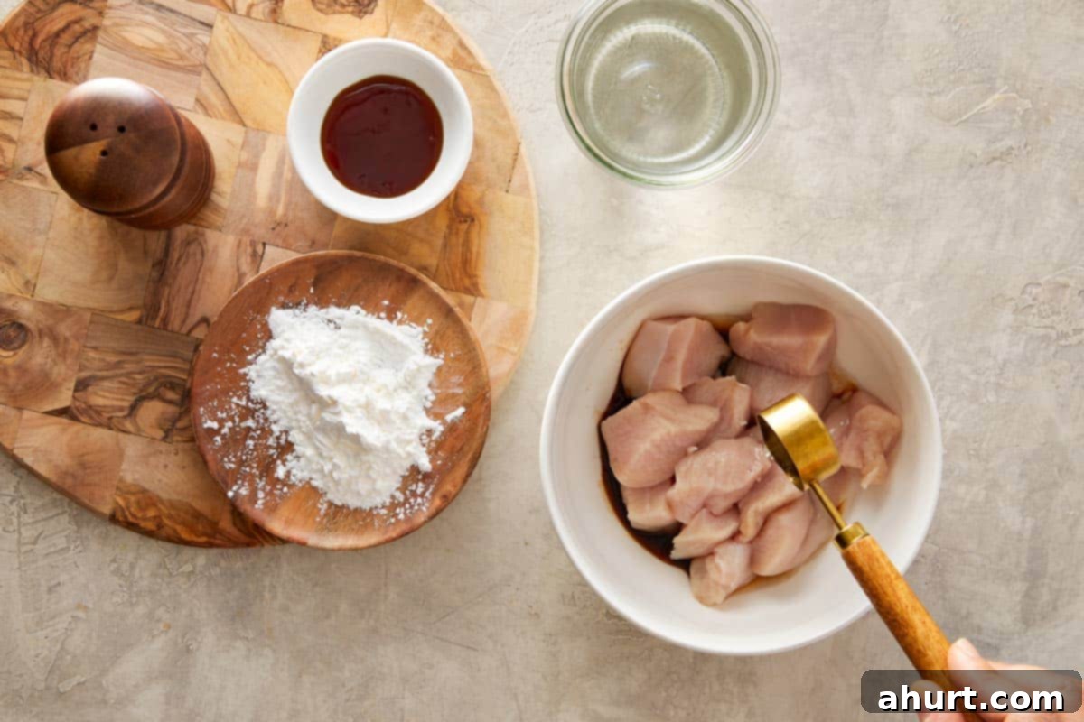 Raw chicken chunks in a bowl with soy sauce, cornstarch, and water.
