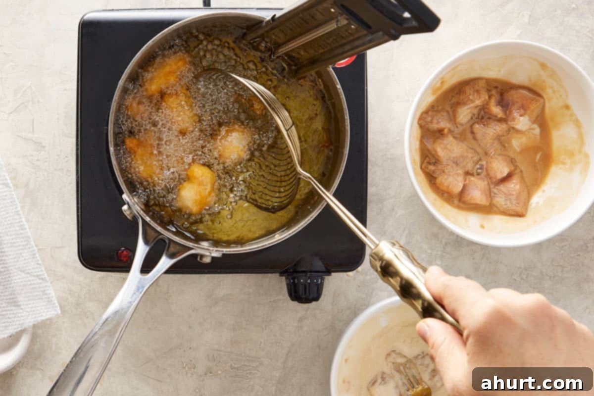 Chicken pieces frying in hot oil in a pot.