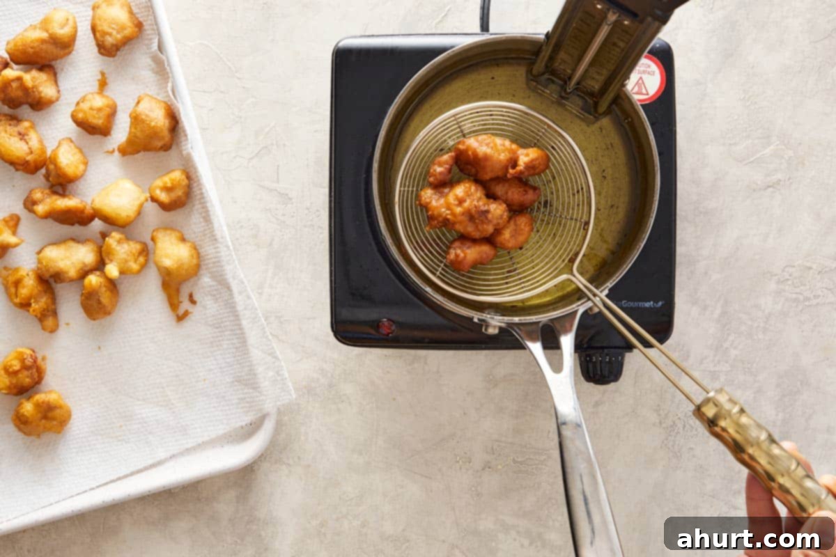 Fried chicken pieces being removed from hot oil to a tray.