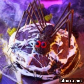 Decadent chocolate layer cake decorated with an edible spiderweb and plastic spiders, perfect for a Halloween centerpiece.