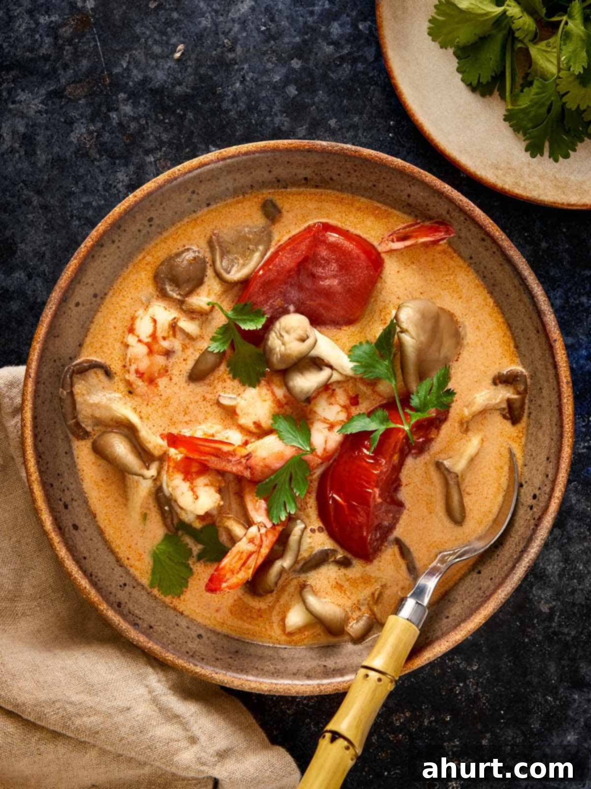 A warm bowl of Tom Yum Kha Soup with shrimp, mushrooms, and tomatoes in a creamy coconut broth, garnished with fresh cilantro.