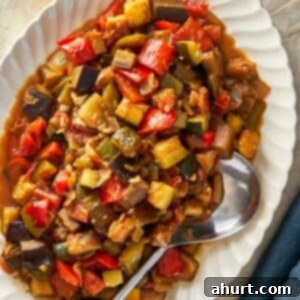 A serving of Ratatouille featuring assorted vegetables, accompanied by a spoon and a glass of red wine.