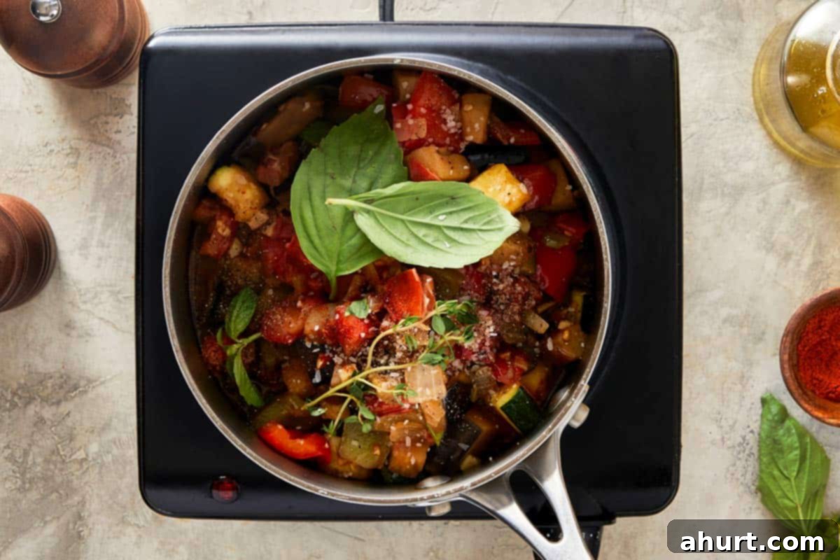 Pot of ratatouille simmering on a stovetop with fresh herbs on top.