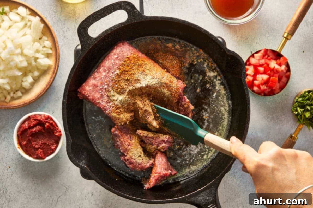 Sizzling ground beef mixed with aromatic spices cooking in a cast iron skillet, browning evenly.