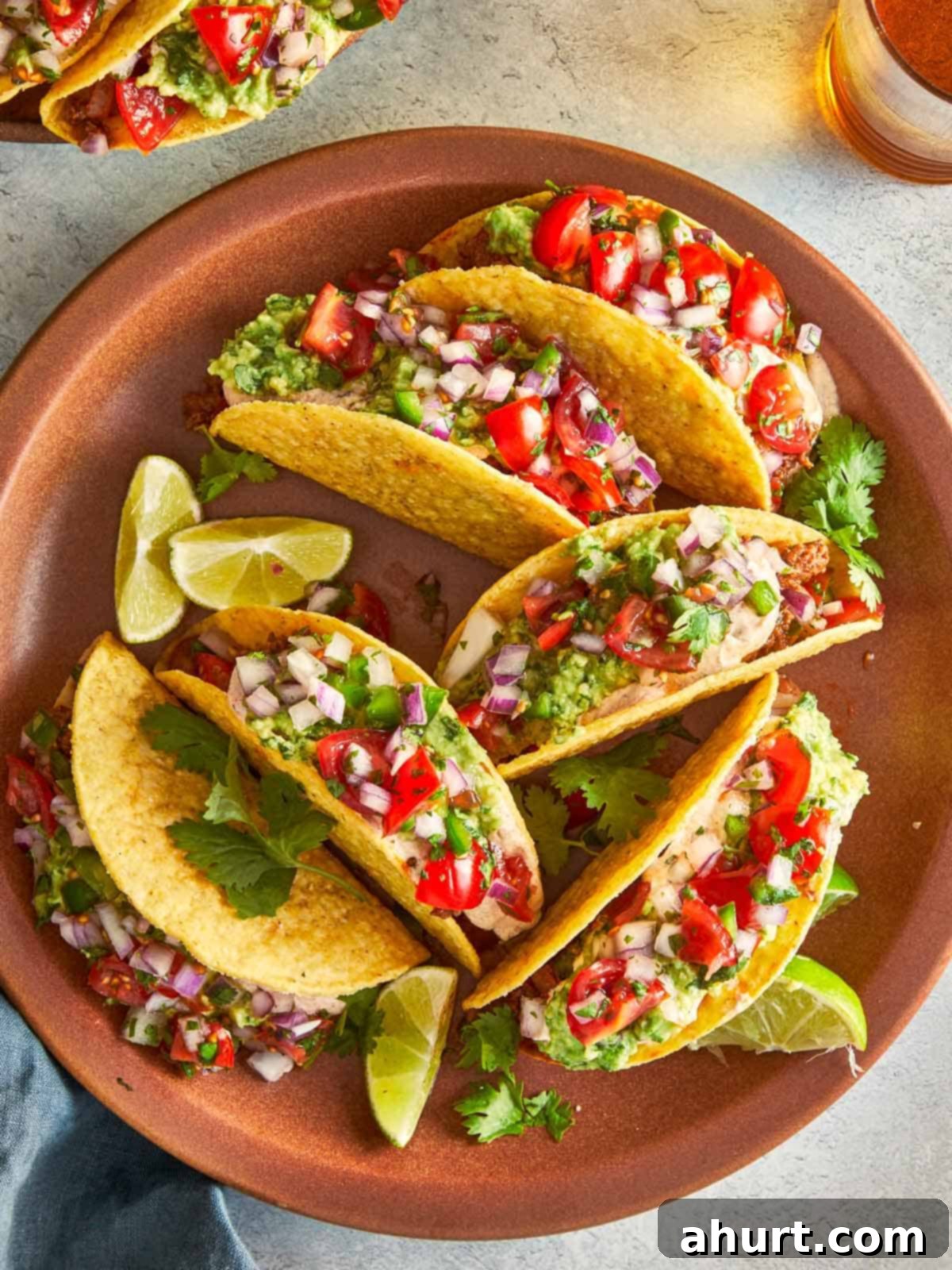 A beautifully arranged plate of ground beef tacos, garnished with fresh guacamole, salsa, and lime wedges, ready to be enjoyed.