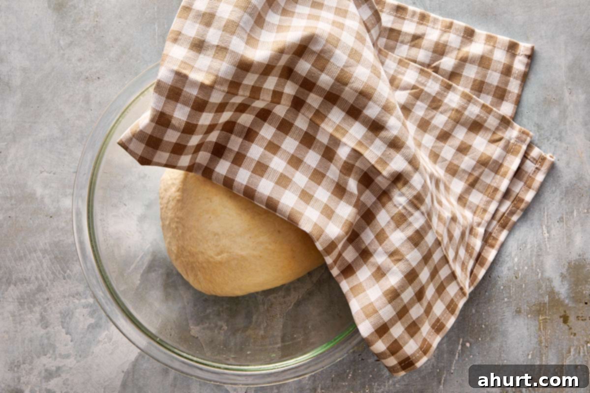 Focaccia-Style Pizza 5 Focaccia dough resting in a bowl, covered with a brown checkered cloth during first rise.
