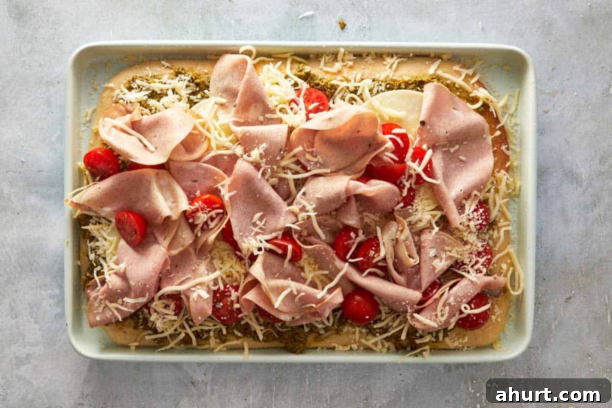 Focaccia-Style Pizza 9 Unbaked pesto focaccia pizza with mortadella, cherry tomatoes, and cheese before going into the oven