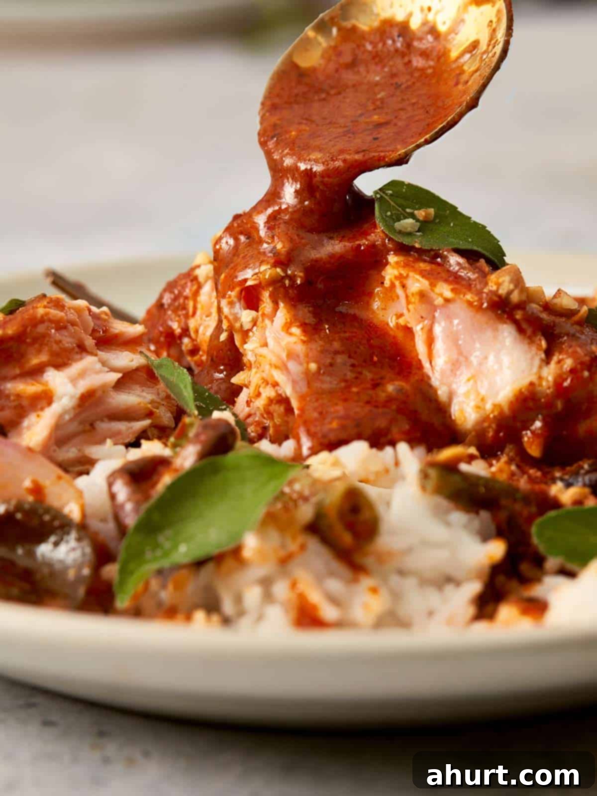 Close-up of golden curry sauce being spooned over salmon and rice, highlighting the creamy texture, kaffir lime leaves, and glossy finish of the Panang curry.