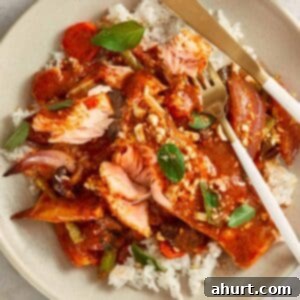 Overhead shot of Salmon Panang Curry served on a plate with jasmine rice. The salmon is coated in a rich red curry sauce, topped with crushed peanuts and fresh Thai basil leaves, with gold cutlery resting on the side.