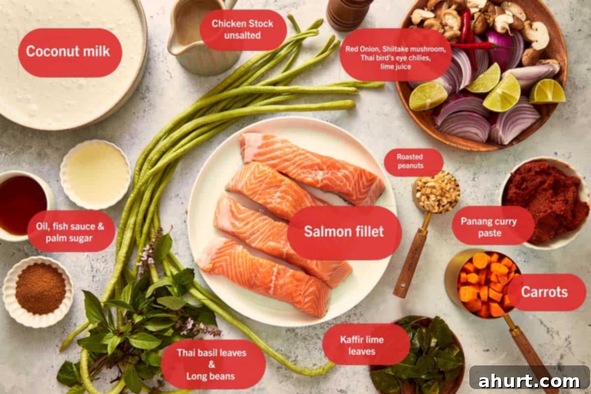 Flat lay of ingredients for Salmon Panang Curry, including salmon fillets, coconut milk, Panang curry paste, kaffir lime leaves, long beans, carrots, red onion, Thai basil, and roasted peanuts, arranged beautifully on a wooden surface.
