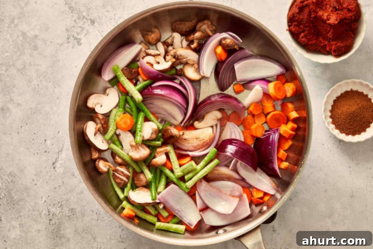 Sliced red onion, carrots, long beans, and shiitake mushrooms sizzling in a pan — the first step to build color and texture for the curry.