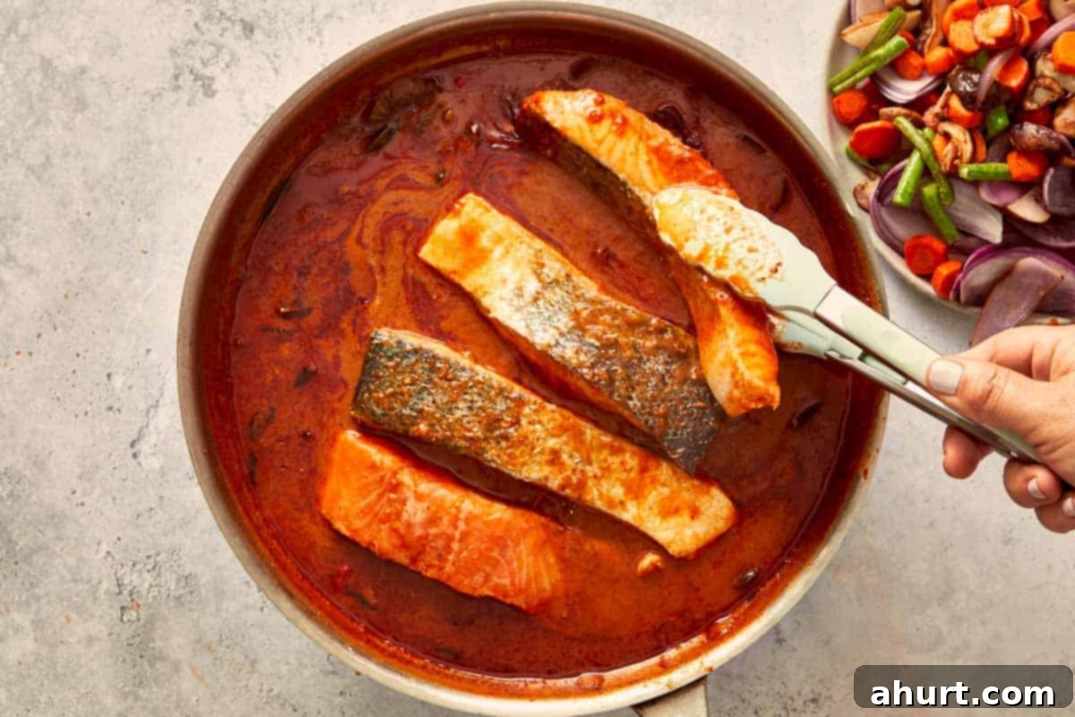 Salmon fillets cooking skin-side down in the simmering Panang curry sauce, slowly turning golden and tender.