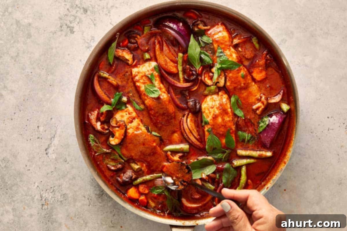Salmon fillets simmering in the rich curry with vegetables, while fresh basil and kaffir lime leaves are stirred in for aroma.
