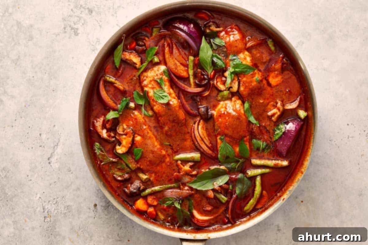 Final simmer of Salmon Panang Curry — a vibrant red sauce filled with salmon, basil, and colorful vegetables ready to serve.