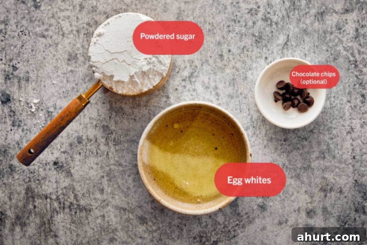 Ingredients for Swiss Meringue Ghosts including powdered sugar, egg whites, and chocolate chips labeled on a gray surface.