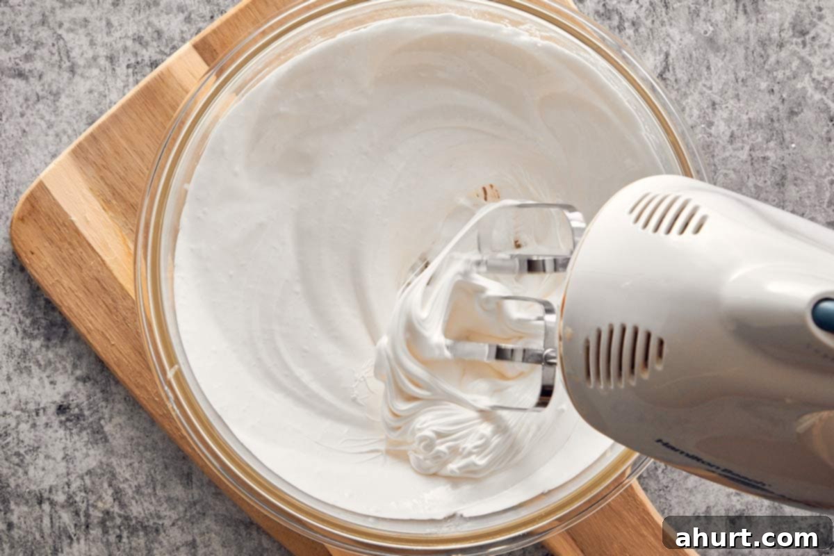 Whipping glossy Swiss meringue with an electric mixer until stiff peaks form.
