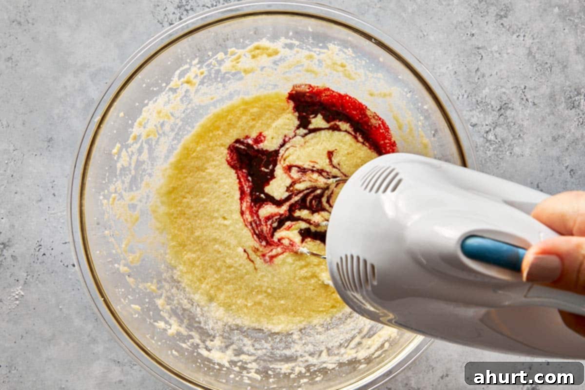 Spooktacular Red Velvet Cake Pops 4 A vibrant red velvet cake batter being mixed in a clear glass bowl, showcasing the rich cocoa and deep red food coloring blending together to create the characteristic hue.