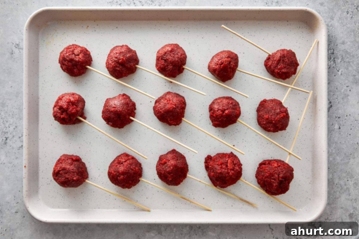 Spooktacular Red Velvet Cake Pops 7 Red velvet cake mixture shaped into smooth, uniform balls, each impaled with a cake pop stick, neatly arranged on a baking tray lined with parchment paper, chilling before coating.