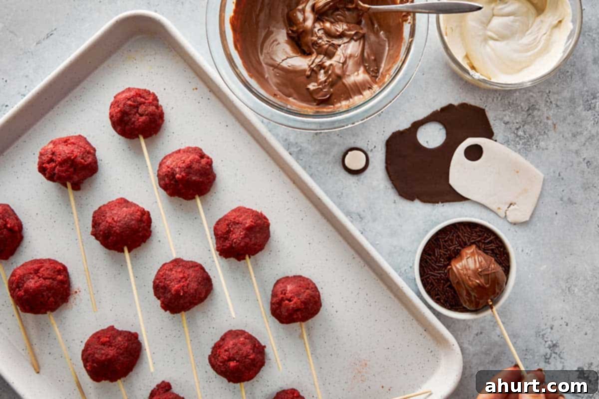 Spooktacular Red Velvet Cake Pops 8 A red velvet cake pop being carefully dipped into a bowl of melted chocolate, with Halloween sprinkles waiting to be added for decoration.
