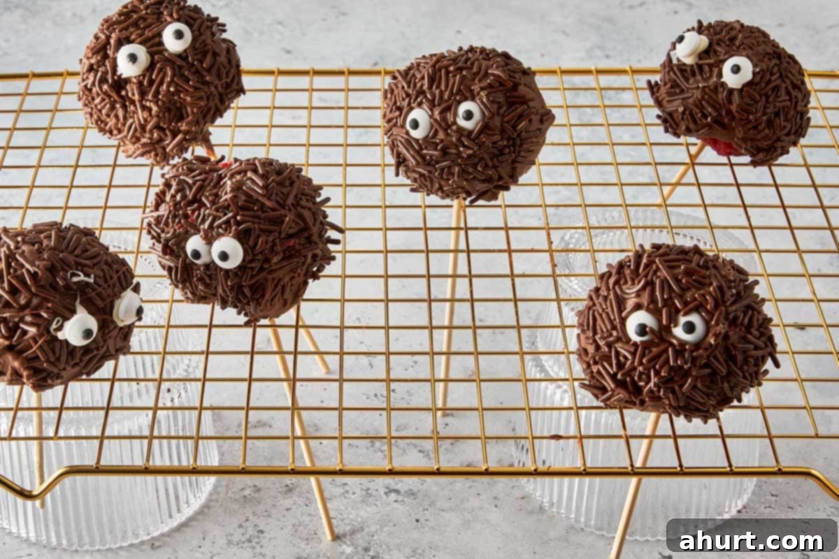 Spooktacular Red Velvet Cake Pops 9 A collection of colorfully decorated monster cake pops, complete with various candy eyes and sprinkles, proudly standing upright in a Styrofoam block, allowing their chocolate coating to set completely.