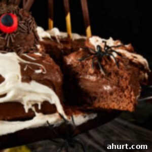 A slice of rich chocolate spider cake on a plate, showing the moist layers and ganache, with a blurred background of the full cake.
