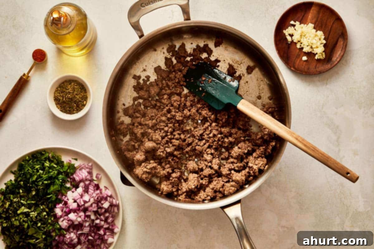 Ground beef cooking in a pan with onions and herbs.