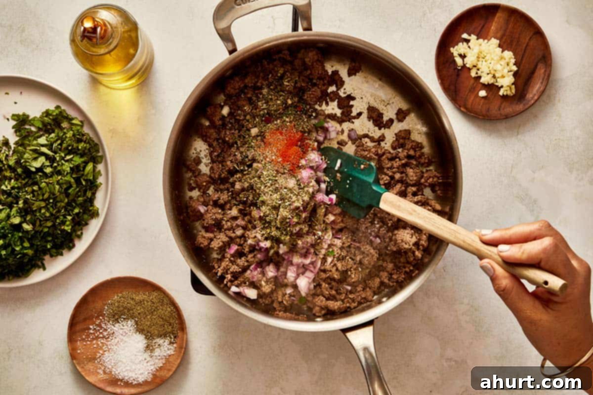 Adding seasoning and chopped onions to browned beef.