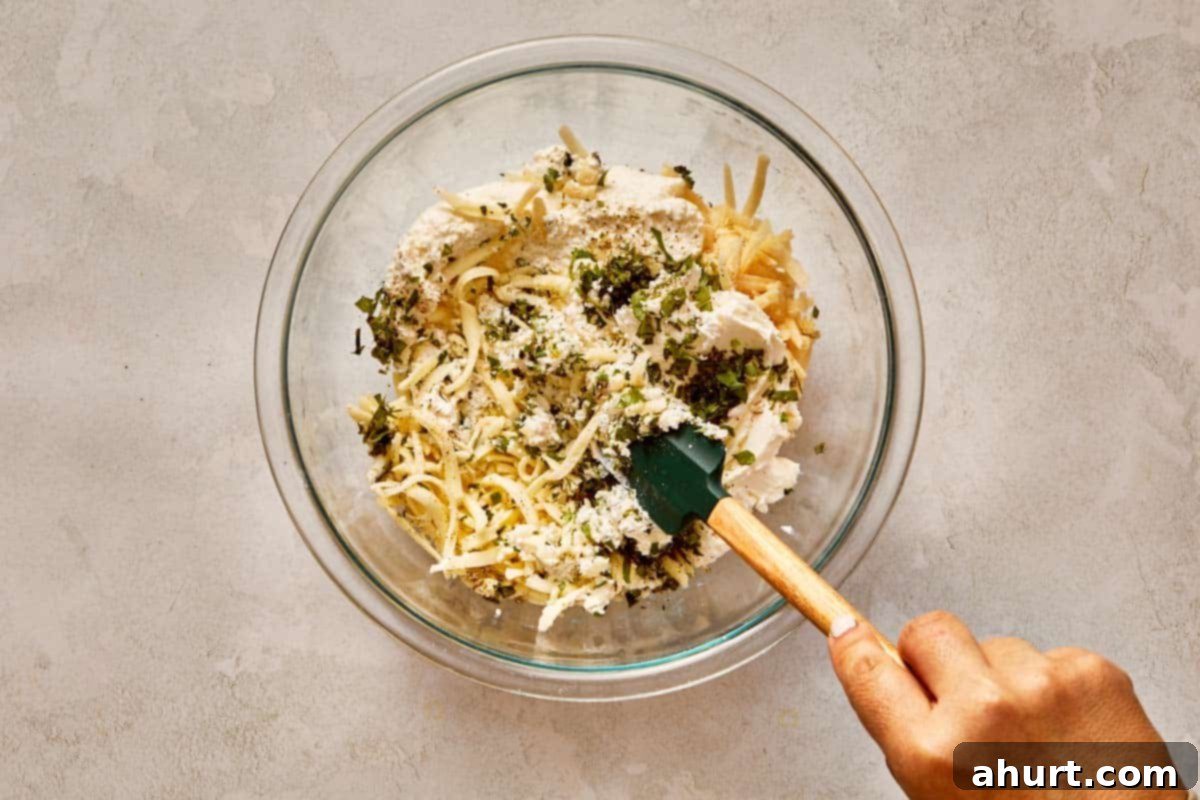 Mixing cheeses, herbs, and seasoning in a glass bowl.