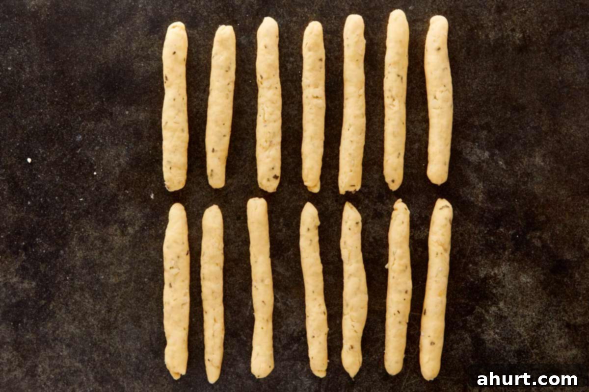 Rows of rolled dough shaped like fingers on a dark surface, ready to transform into witchy grissini.
