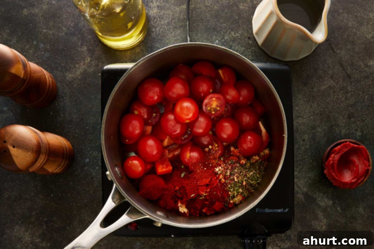 Overhead shot of cherry tomatoes, diced red capsicum, garlic, paprika, and herbs in a saucepan with olive oil ready to cook.