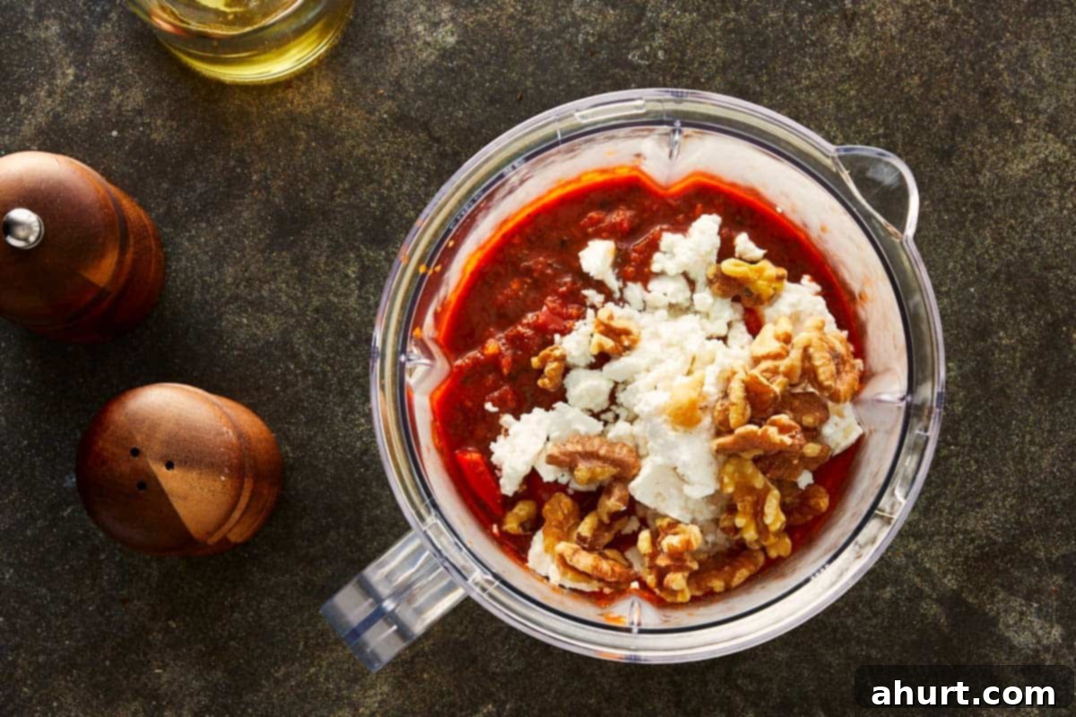 Blender filled with roasted red sauce, feta cheese, and walnuts ready to blend into a smooth, creamy dip.