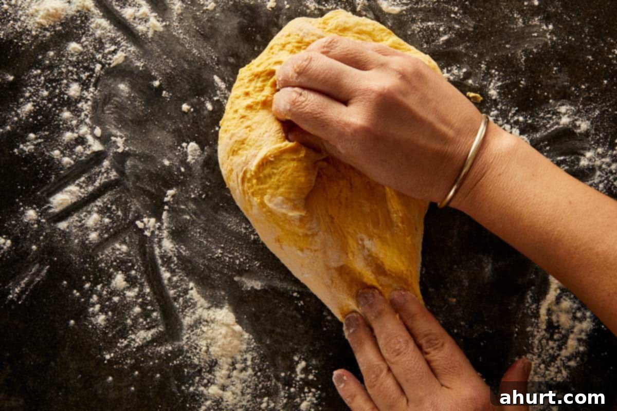 Hands kneading soft pumpkin bread dough on a floured surface.
