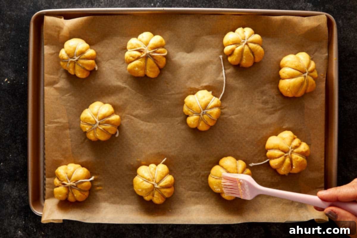 Pumpkin-shaped dough balls tied with kitchen twine and brushed with egg wash on a baking tray.