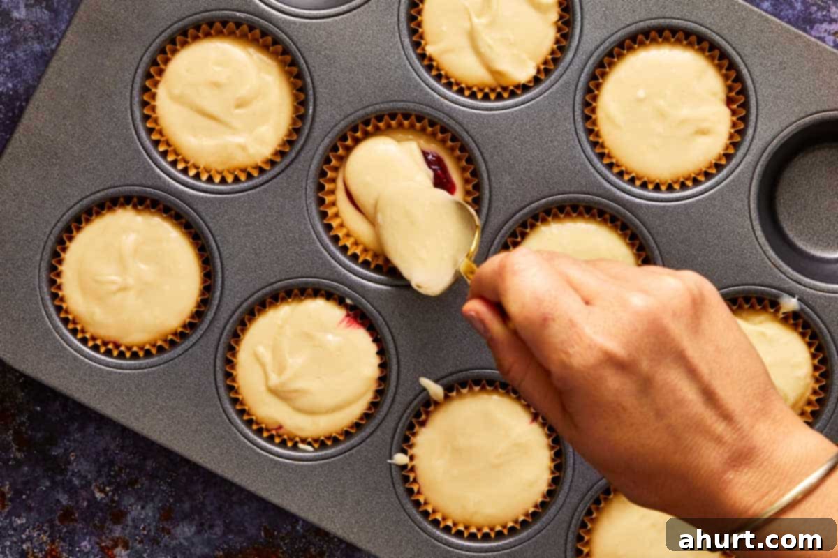 Hand spooning muffin batter into paper liners, adding a frozen raspberry insert in the center of each muffin tin. Creating the bloody surprise.