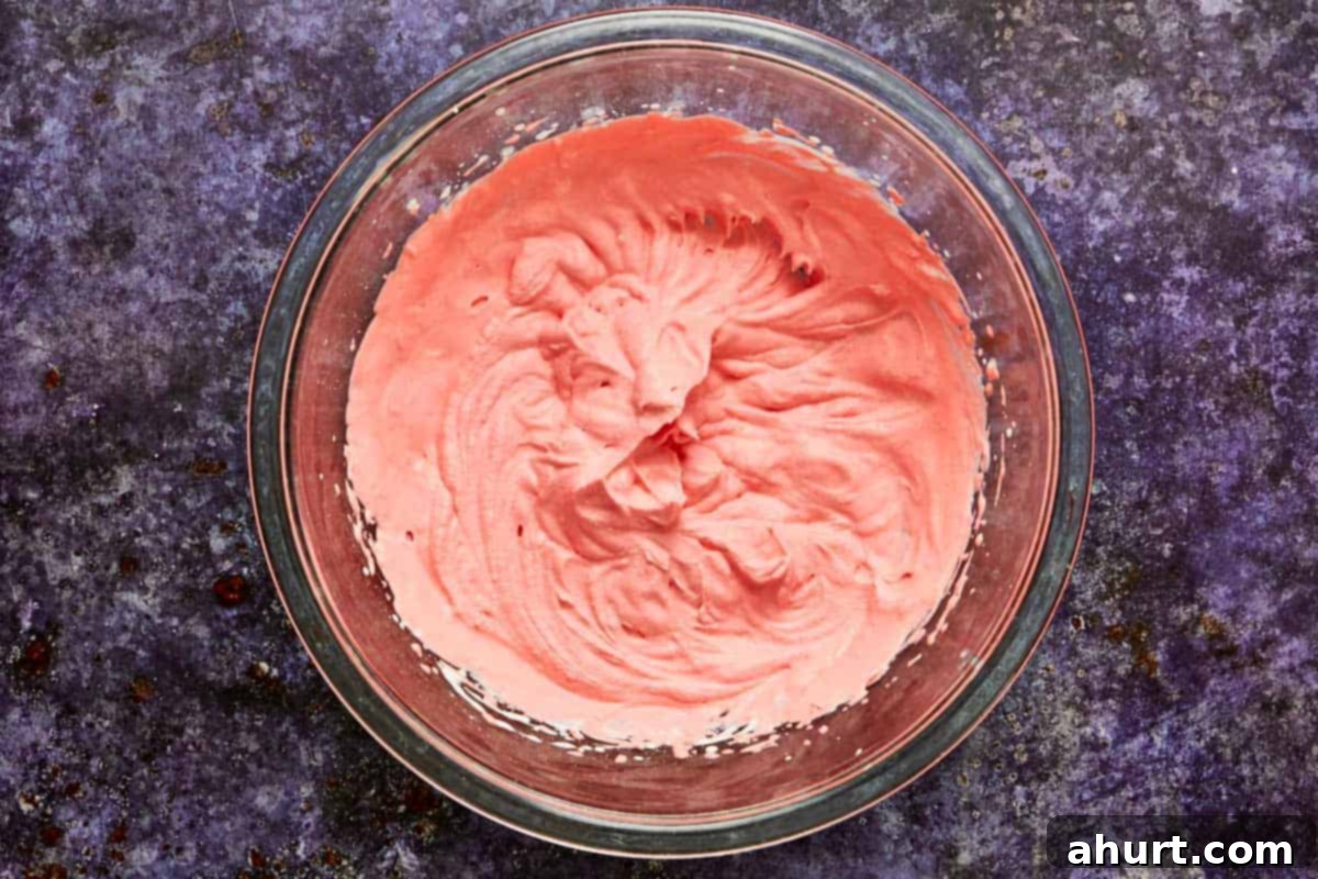 Bowl of pink whipped cream topping, made with heavy cream, vanilla, and red food coloring, ready for piping. Essential for the spooky effect.