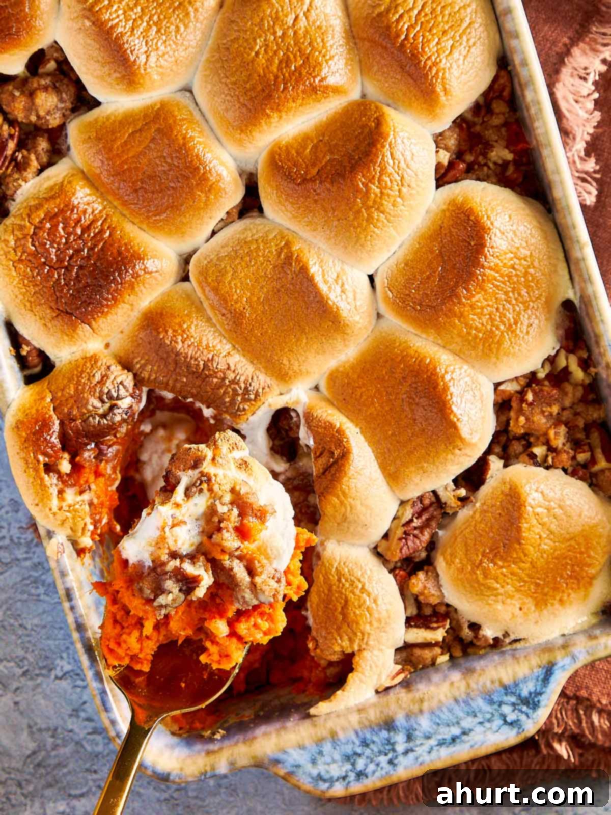 Sweet potato casserole with toasted marshmallows on top, with a spoon lifting a scoop showing the creamy sweet potato layer and crunchy pecan streusel.